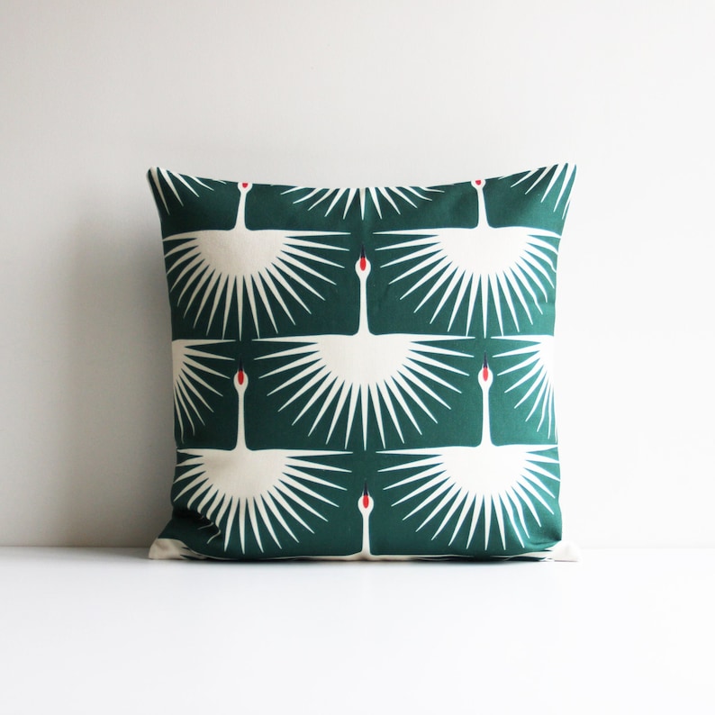 May include: A green throw pillow with a white crane pattern. The crane design features a stylized sunburst pattern.