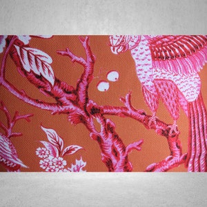 May include: A pink and white parrot perched on a branch of a pink and white tree. The background is a solid orange color.