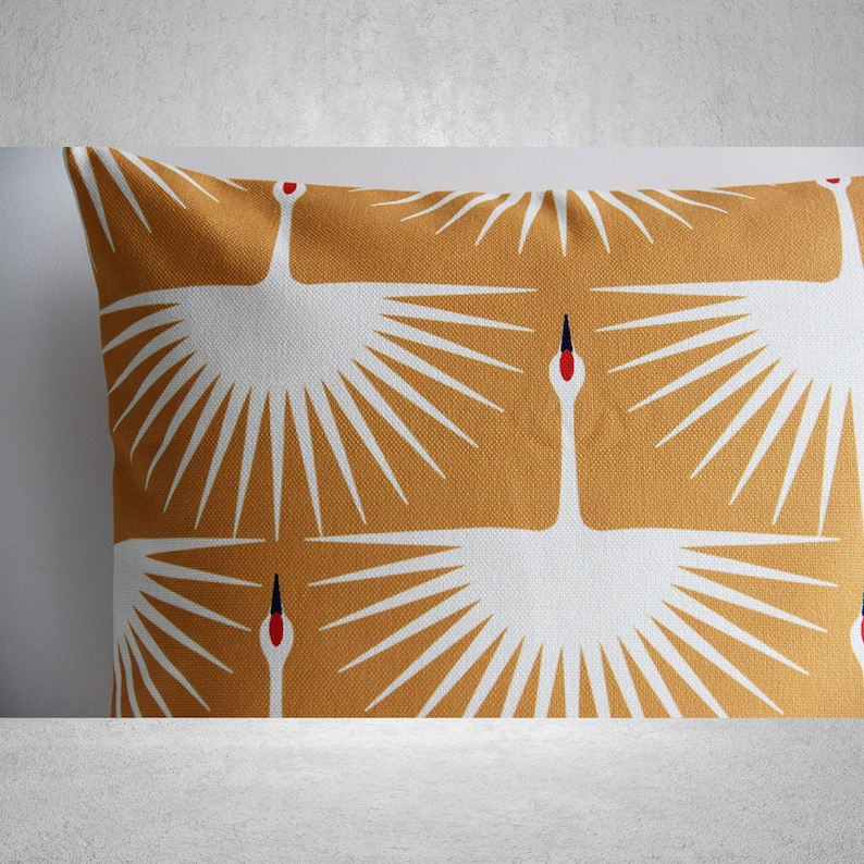 May include: A mustard yellow throw pillow with a white crane design. The crane has a red beak and black eyes. The design is repeated on the pillow.
