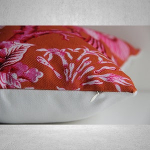 May include: A close-up of a rust-colored pillow with a white zipper. The pillow has a pink and white floral pattern.