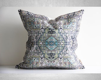May include: A decorative throw pillow with a white background and a colorful, intricate pattern in shades of blue, green, and brown. The pattern resembles a traditional rug or tapestry.