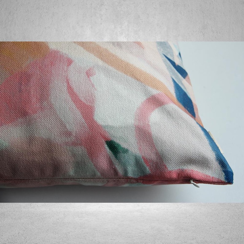 May include: A pink, blue, and green abstract pattern printed on a white pillow cover. The pillow has a zipper closure.