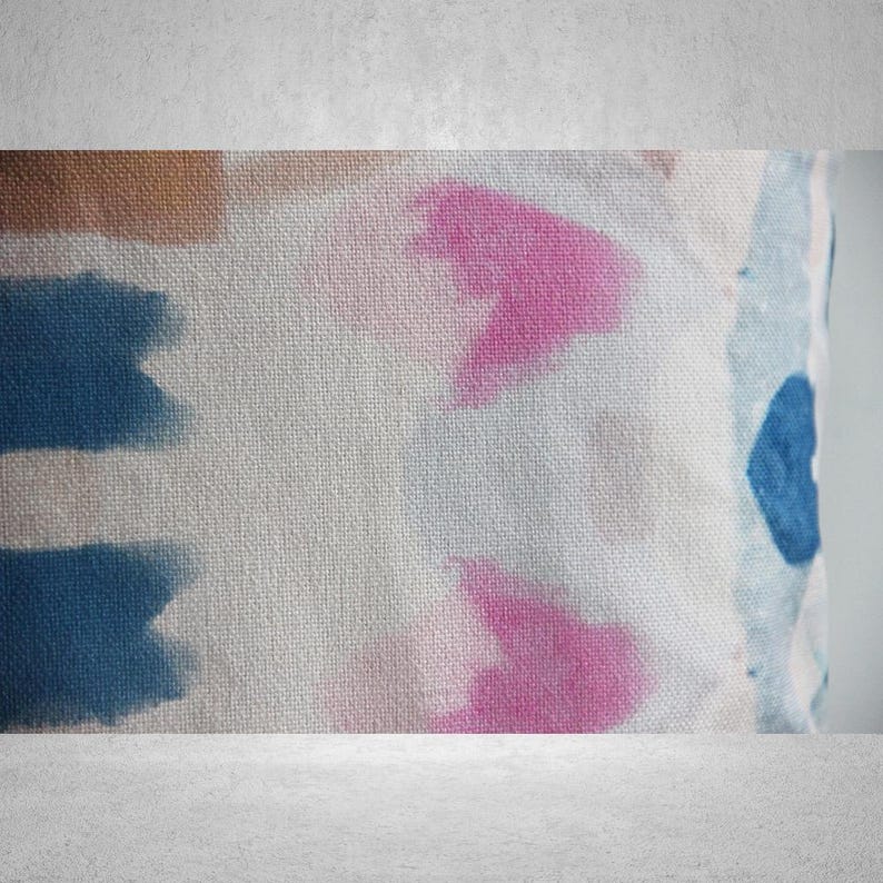 May include: A white fabric pillow with a blue and pink tie-dye pattern. The pillow has a textured surface and is made of a soft, comfortable material.