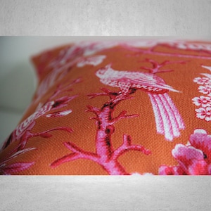 May include: Orange throw pillow with a pink and white floral pattern featuring birds and branches.