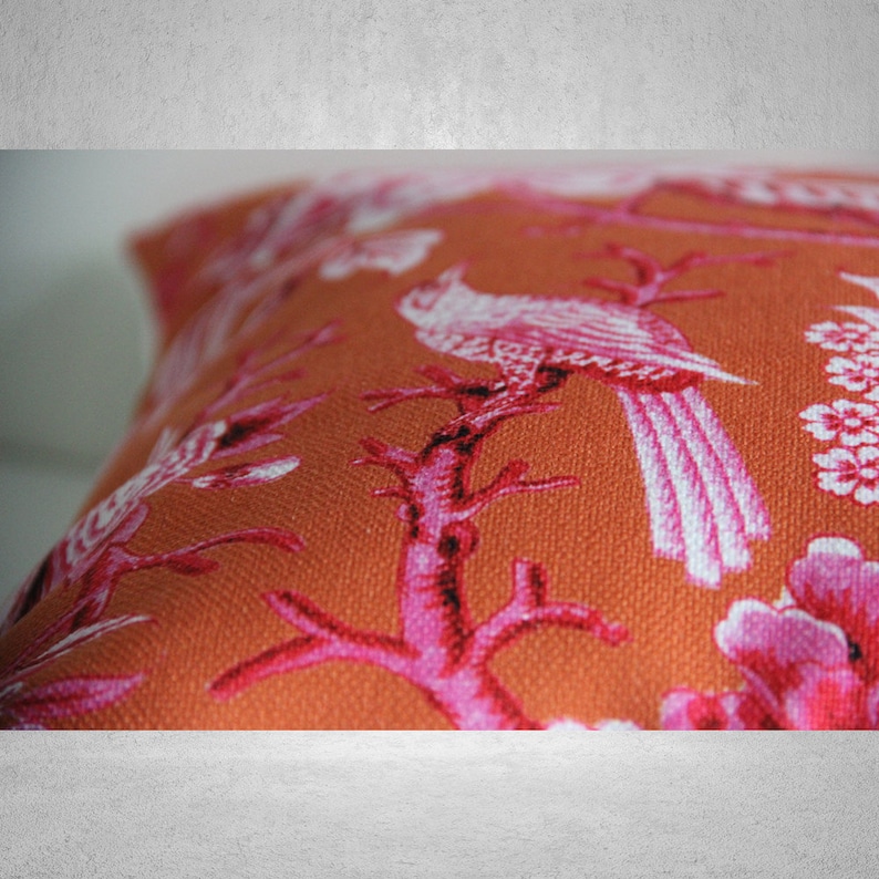 May include: Orange throw pillow with a pink and white floral pattern featuring birds and branches.