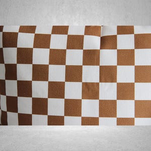 May include: A brown and white checkered pillow with a subtle texture. The pillow is made of fabric and has a square shape.