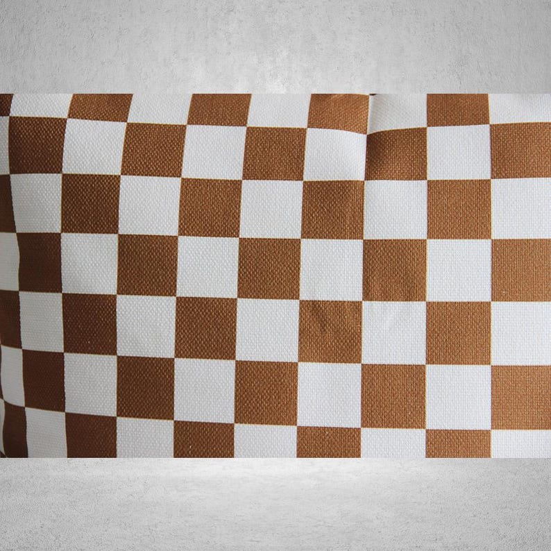 May include: A brown and white checkered pillow with a subtle texture. The pillow is made of fabric and has a square shape.