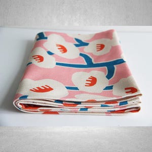 May include: Folded pink fabric with a white floral pattern and blue stems. The flowers have red centers.