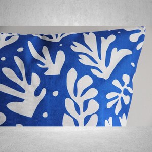 May include: Blue and white throw pillow with a geometric pattern of stylized leaves. The pillow is made of a soft, textured fabric.
