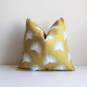 Può includere: Cuscino decorativo giallo senape con un motivo a ventaglio bianco e azzurro. Il cuscino quadrato è realizzato in tessuto. Il design presenta diverse illustrazioni di palme a ventaglio, creando un tema tropicale.