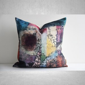 May include: A colorful abstract pillow cover with a geometric design in shades of blue, red, purple, yellow, and green. The design features black lines and scribbles.