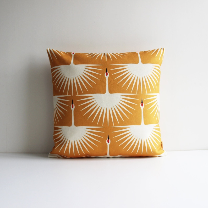 May include: A yellow throw pillow with a white crane pattern. The crane design is repeated in a geometric pattern.