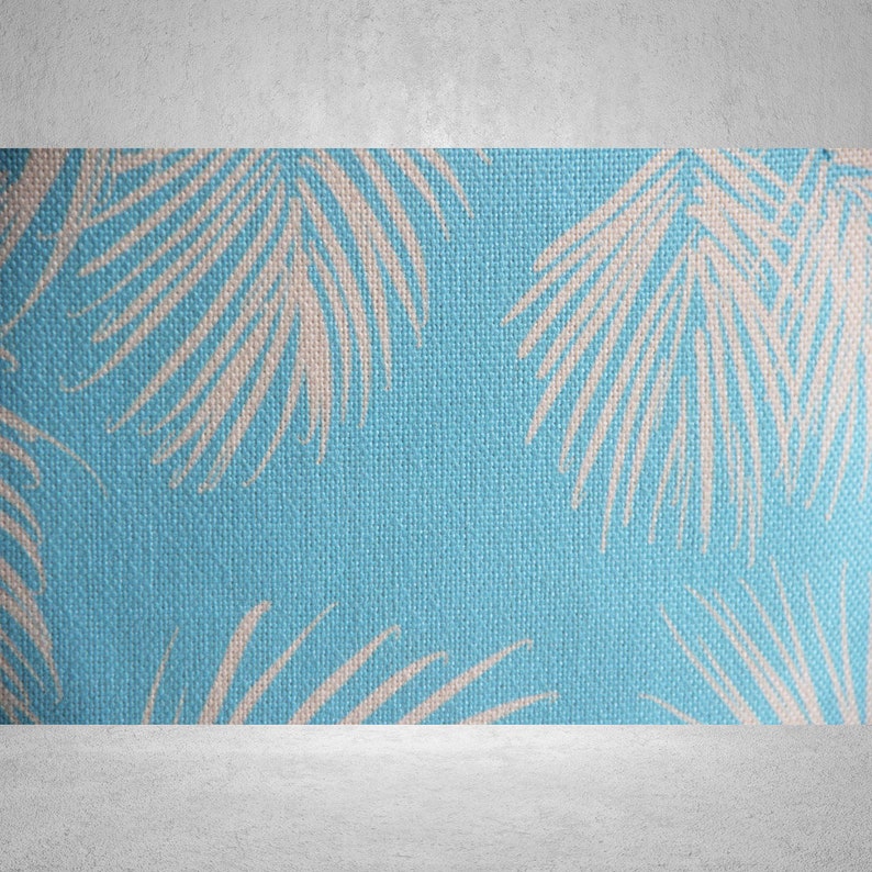 May include: Close-up of a blue fabric with a repeating pattern of white palm leaves. The fabric has a textured appearance, with the leaves arranged in a scattered design. The background is a solid light blue.
