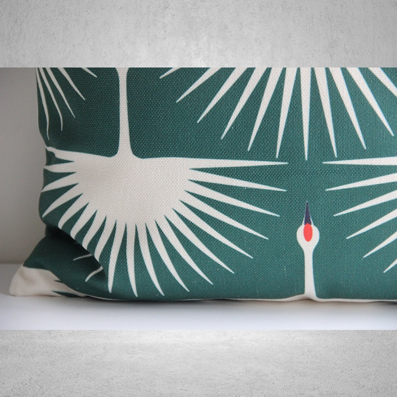 May include: A green and white throw pillow with a stylized design of a crane with its wings spread. The crane is white with a red beak and black eyes. The background is a deep green.