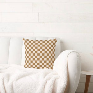May include: A white couch with a brown and white checkered throw pillow. The couch is covered in a white blanket.