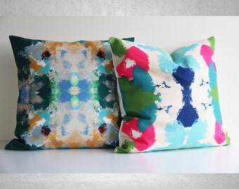 May include: Two decorative throw pillows with abstract patterns in shades of blue, green, pink, and yellow. The pillows are made of a soft, textured fabric.