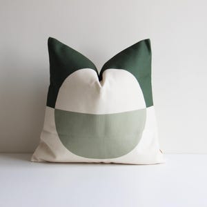 May include: A green and white geometric patterned cushion. The cushion has a large circle design with a green top and a lighter green bottom.