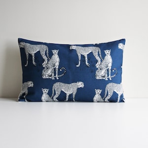 May include: A blue rectangular pillow with a white cheetah print pattern. The pillow features multiple cheetahs in various poses, including standing, sitting, and walking.