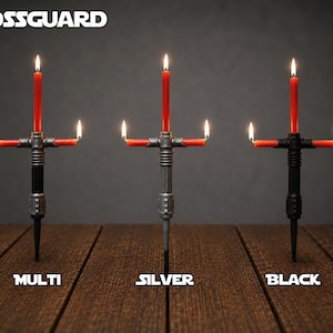 May include: Three candle holders shaped like crossguard hilts, each holding three lit red taper candles. The holders are labeled Multi, Silver, and Black, with the text CROSSGUARD at the top. The designs feature metallic-style handles.