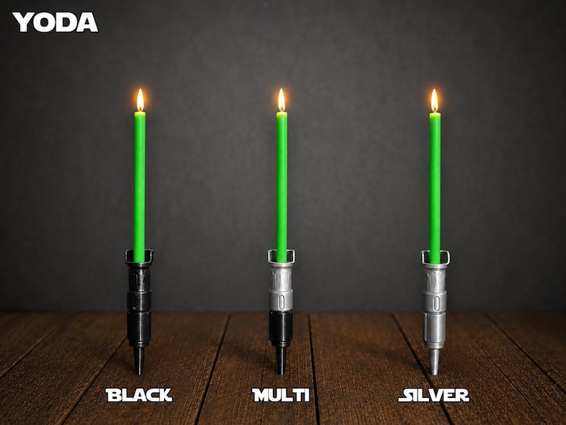 May include: Three lit green taper candles held in vertical holders shaped like lightsaber hilts. The left holder is black, the center is a multi-colored black and silver, and the right is silver. The text YODA appears at the top left, with BLACK, MULTI, and SILVER labels below each candle.