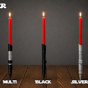 May include: Three lit red taper candles held in cylindrical holders with detailed metallic textures. The holders are labeled Multi, Black, and Silver. The word VADER appears in the top left corner. The holders feature segmented designs with ridges and grooves, standing upright on a wooden surface.