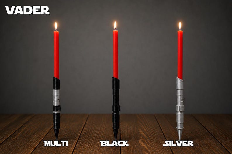 May include: Three lit red taper candles held in cylindrical holders with detailed metallic textures. The holders are labeled Multi, Black, and Silver. The word VADER appears in the top left corner. The holders feature segmented designs with ridges and grooves, standing upright on a wooden surface.