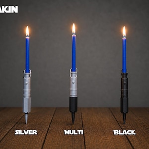 May include: Three lit blue taper candles held in cylindrical holders resembling lightsaber hilts. The holders are labeled as silver, multi, and black. The text ANAKIN appears in the top left corner, with labels silver, multi, and black below.