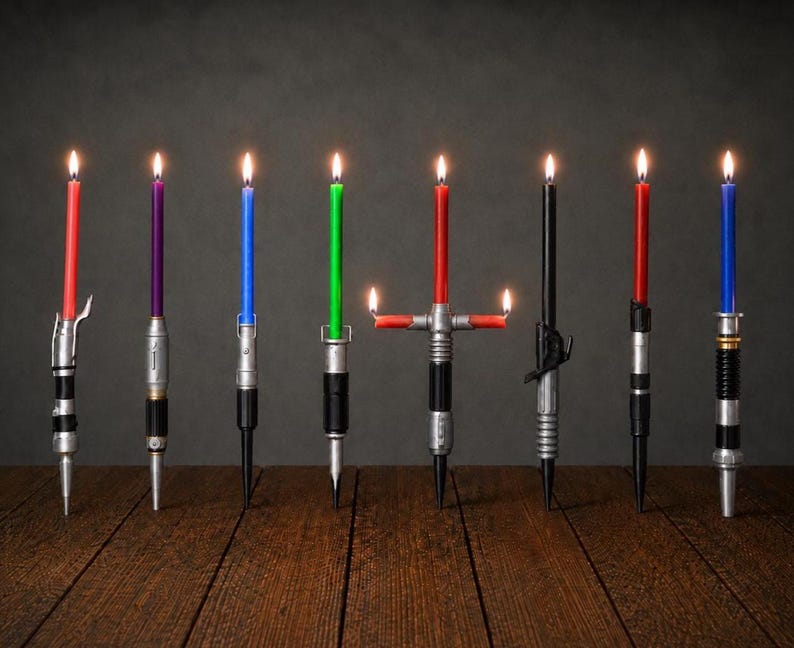 May include: Eight lit taper candles in various colors including red, purple, blue, green, and black, each held in a metallic, cylindrical base designed to resemble a sci-fi weapon handle. One candle features a cross-guard design with two side flames.
