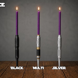 May include: Three lit purple taper candles held in vertical holders designed like lightsaber hilts. The holders are labeled MACE, with individual labels for BLACK, MULTI, and SILVER finishes. The hilts feature cylindrical, metallic-looking details.