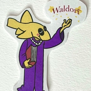 May include: A cartoon character with a yellow fish head wearing a purple robe and holding a book. The character is holding out a hand with stars coming out of it. The word "Waldorf" is written in red above the character.