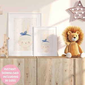 Op de afbeelding: Twee ingelijste aquarelprints van een konijn met een blauwe strik, tegen een pastel achtergrond met confetti. Een knuffel leeuw en houten giraffe staan op een houten kast. De tekst "INSTANT DOWNLOAD INCLUDING 35 SIZES" is inbegrepen.