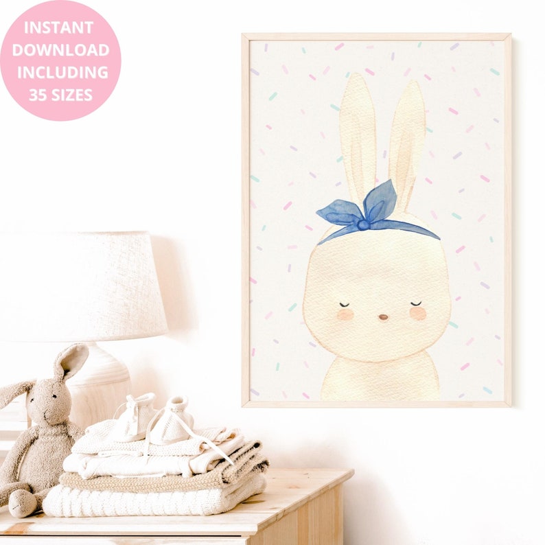 Op de afbeelding: Een ingelijste aquarelprint van een konijn met een blauwe strik. Het konijn is cr&egrave;mekleurig met gesloten ogen en roze wangen. De achtergrond is wit met kleurrijke confetti. Tekst: "DIRECT DOWNLOAD INCLUSIEF 35 MATEN".