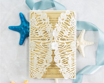 May include: A white laser cut wedding invitation with a seashell and ocean wave design. The invitation is on a beige background with blue and yellow starfish.