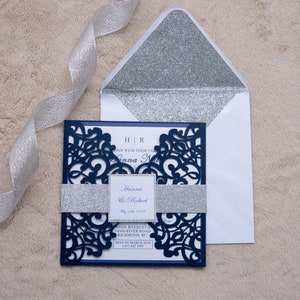 May include: Navy blue wedding invitation with a silver glitter band and a laser cut design. The invitation includes the names Hanna & Robert, the date May 16, 2019, and the location of the wedding. The RSVP information is also included.