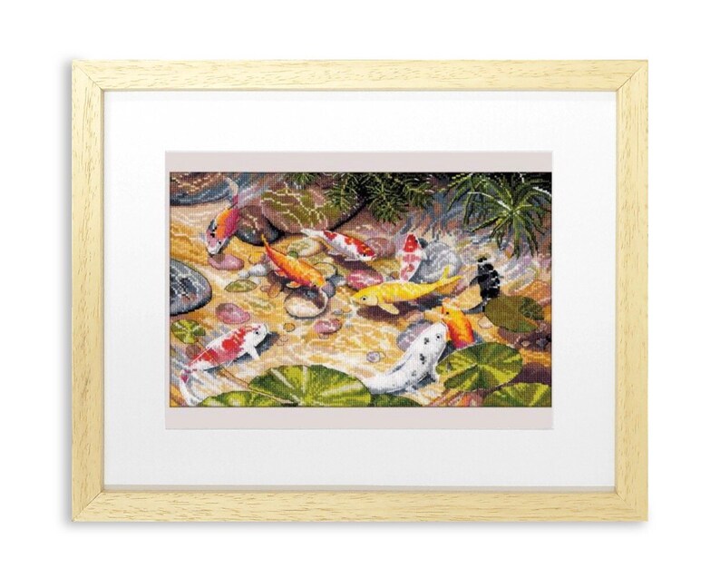 May include: Framed cross-stitch artwork depicting a pond scene with colorful koi fish. The fish are orange, yellow, white, and black, swimming among lily pads and rocks. The artwork is framed in a light wood frame.
