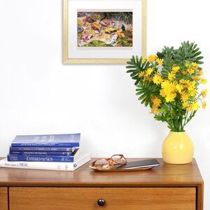 May include: A framed artwork depicting koi fish in a pond, with orange, white, and black markings. The artwork is displayed on a wooden table with books, a tray with glasses, and a yellow vase with yellow flowers.