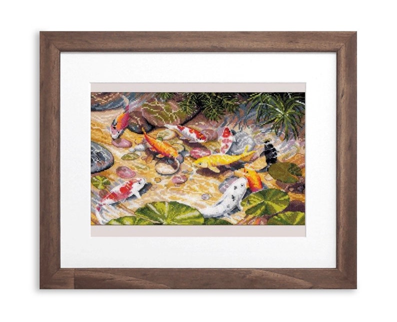 May include: A framed cross-stitch artwork depicting a pond scene with colorful koi fish. The fish are orange, white, yellow, and black, swimming among lily pads and rocks. The frame is a dark brown wood.