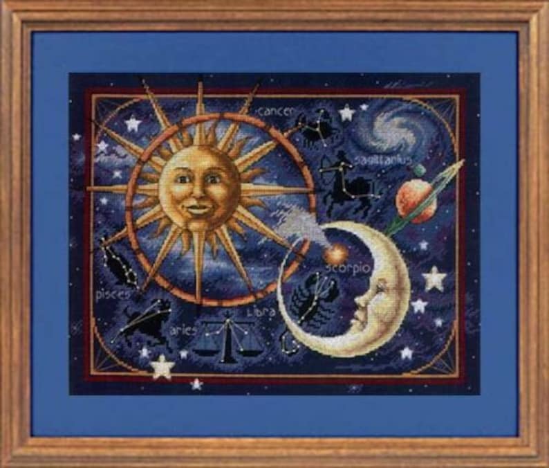 May include: A cross-stitch embroidery depicting the zodiac signs in a celestial scene with a sun and moon. The sun and moon are stylized with faces and the zodiac signs are arranged around them. The background is a dark blue with stars.