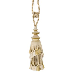 May include: A beige and gold tassel with a tiered top and a long cord. The tassel is made of multiple layers of fringe and has a decorative knot at the top of the cord.