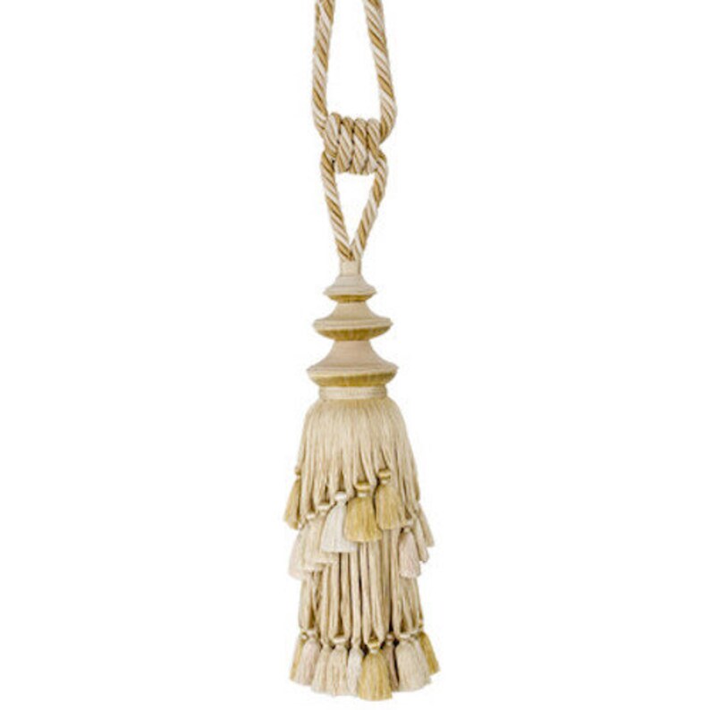 May include: A beige and gold tassel with a tiered top and a long cord. The tassel is made of multiple layers of fringe and has a decorative knot at the top of the cord.