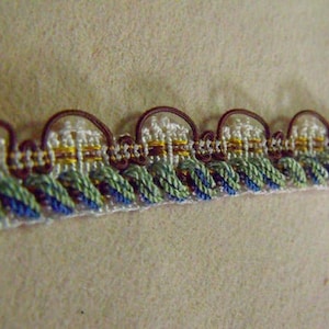 May include: Close-up of a brown, green, and blue trim with a white and gold pattern. The trim has a scalloped edge.