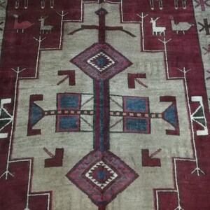May include: A traditional rug with a geometric design in shades of red, blue, and white. The rug features a central diamond shape with a cross pattern and stylized animal figures in the border.