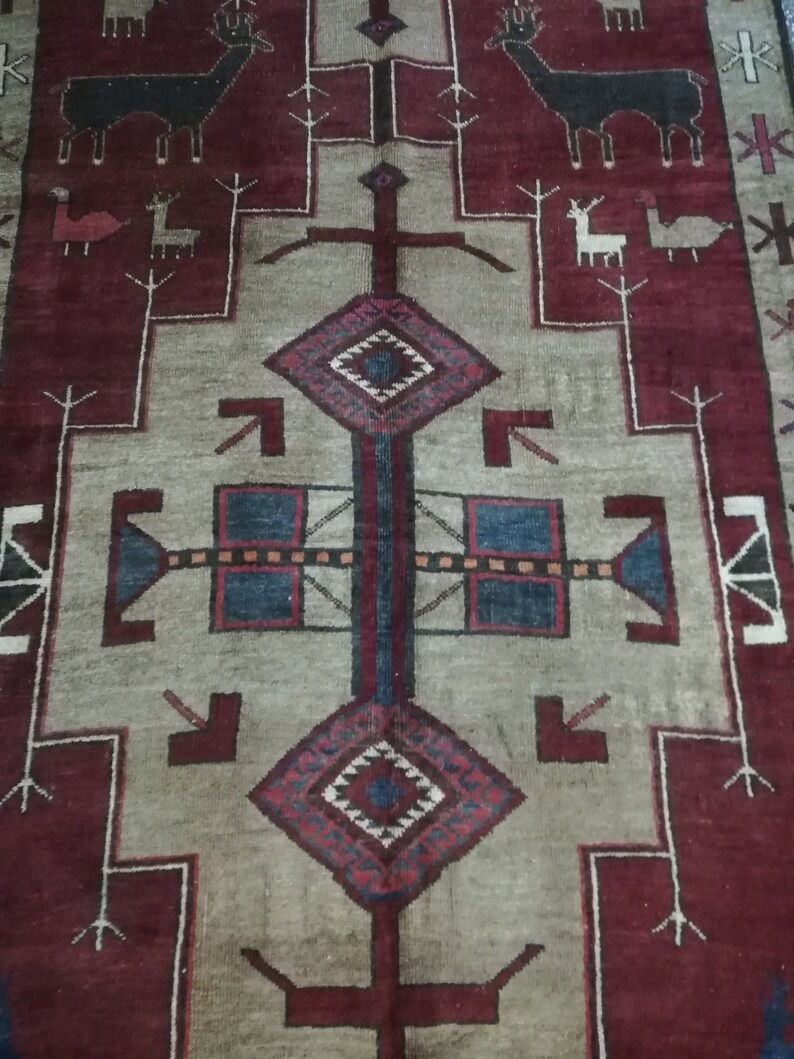 May include: A traditional rug with a geometric design in shades of red, blue, and white. The rug features a central diamond shape with a cross pattern and stylized animal figures in the border.
