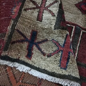 May include: Close-up of a vintage rug with a geometric pattern in shades of red, brown, and white. The rug has a fringe border and is made of wool.