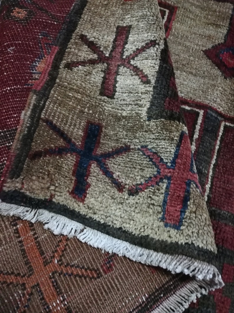 May include: Close-up of a vintage rug with a geometric pattern in shades of red, brown, and white. The rug has a fringe border and is made of wool.
