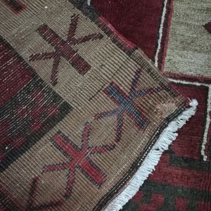 May include: Close-up of a brown and red patterned rug with a white fringe. The rug has a geometric design with stars and other shapes.