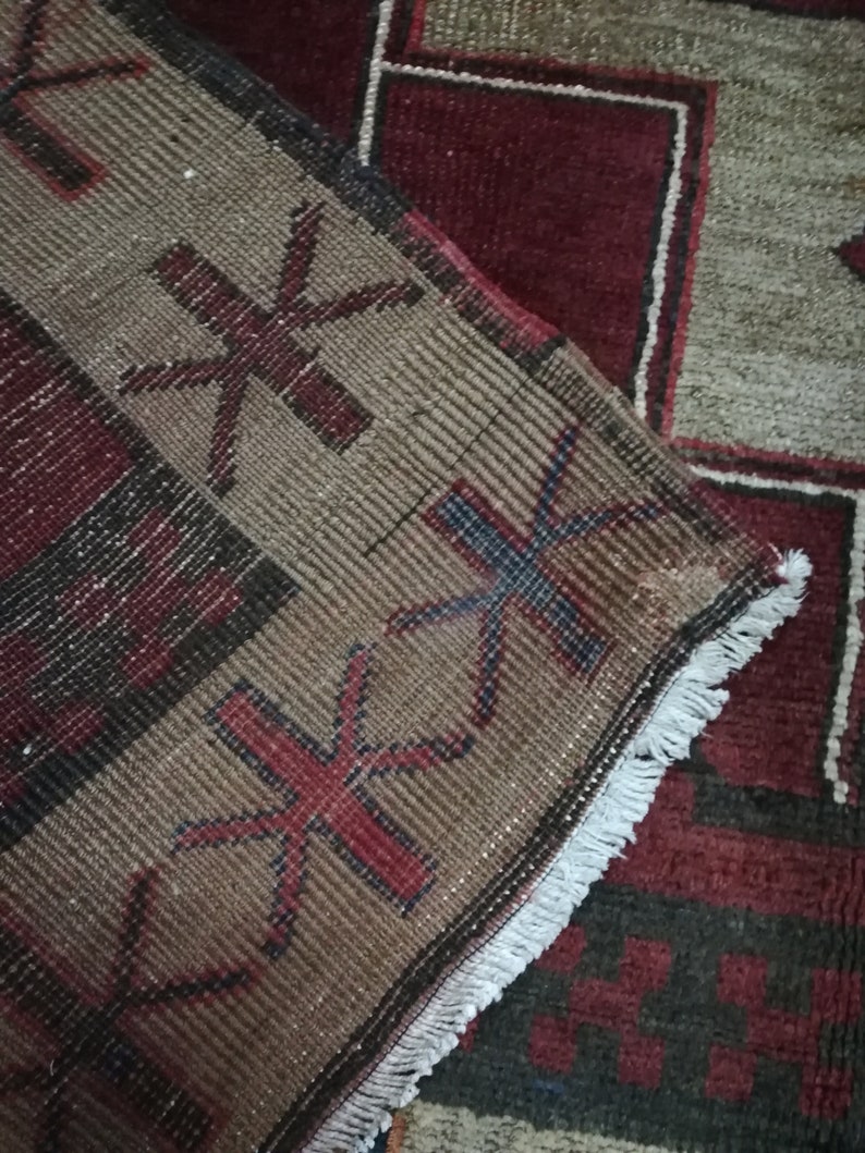 May include: Close-up of a brown and red patterned rug with a white fringe. The rug has a geometric design with stars and other shapes.