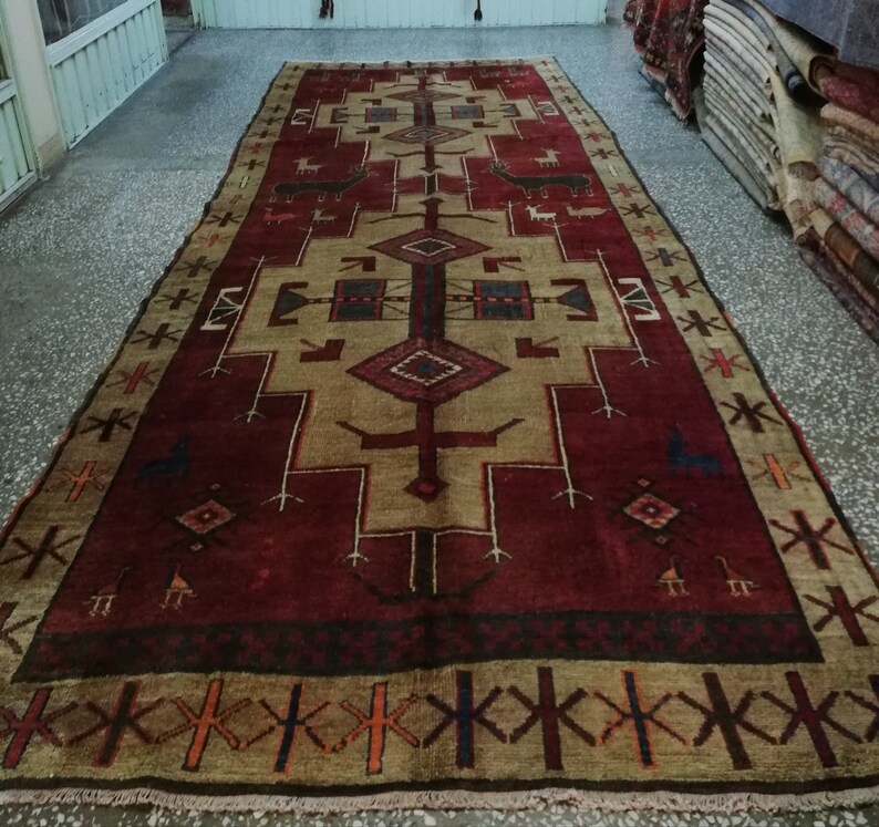 May include: A traditional Turkish rug with a red and beige color scheme. The rug features a geometric pattern with a central diamond shape and intricate details. The rug has a fringe border.