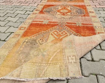 May include: A vintage Turkish rug with a faded orange, red, and beige color scheme. The rug has a traditional geometric pattern and is folded in half, revealing the underside.