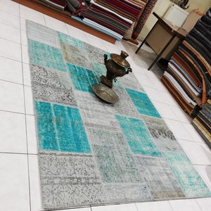 May include: A teal and grey patchwork rug with a traditional design. The rug is laid out on a tiled floor with a decorative metal samovar in the centre.